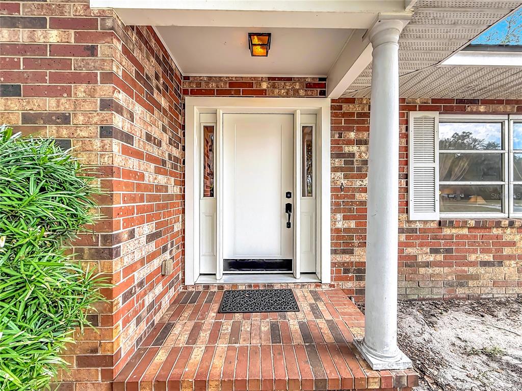 A brick porch leads to a white front door with sidelights and a single column — 1112 CABALLO ROAD, LEESBURG, FL