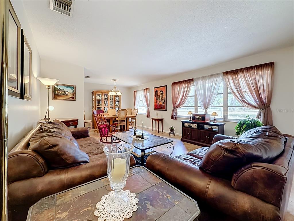 A living room with brown leather sofas, a coffee table, and an adjacent dining area — 1112 CABALLO ROAD, LEESBURG, FL