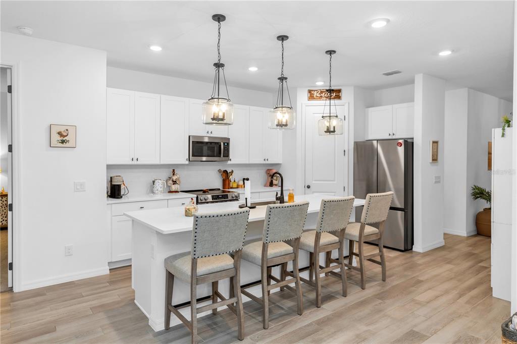A modern kitchen features white cabinetry, a central island with four chairs, and stainless appliances — 1450 ARBOR HILL DRIVE, DELTONA, FL