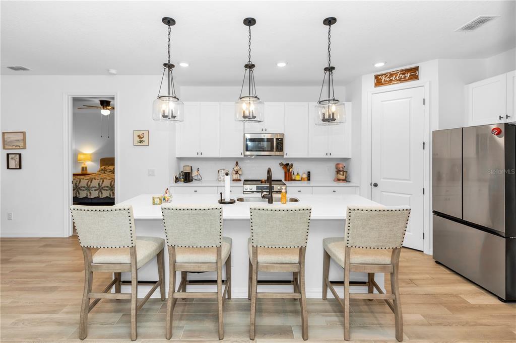 A modern kitchen features white cabinetry, a large island with four chairs, and stainless appliances — 1450 ARBOR HILL DRIVE, DELTONA, FL