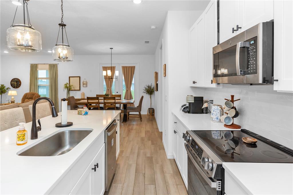 A modern kitchen features white cabinets, quartz countertops, stainless steel appliances, and wood-look tile flooring — 1450 ARBOR HILL DRIVE, DELTONA, FL