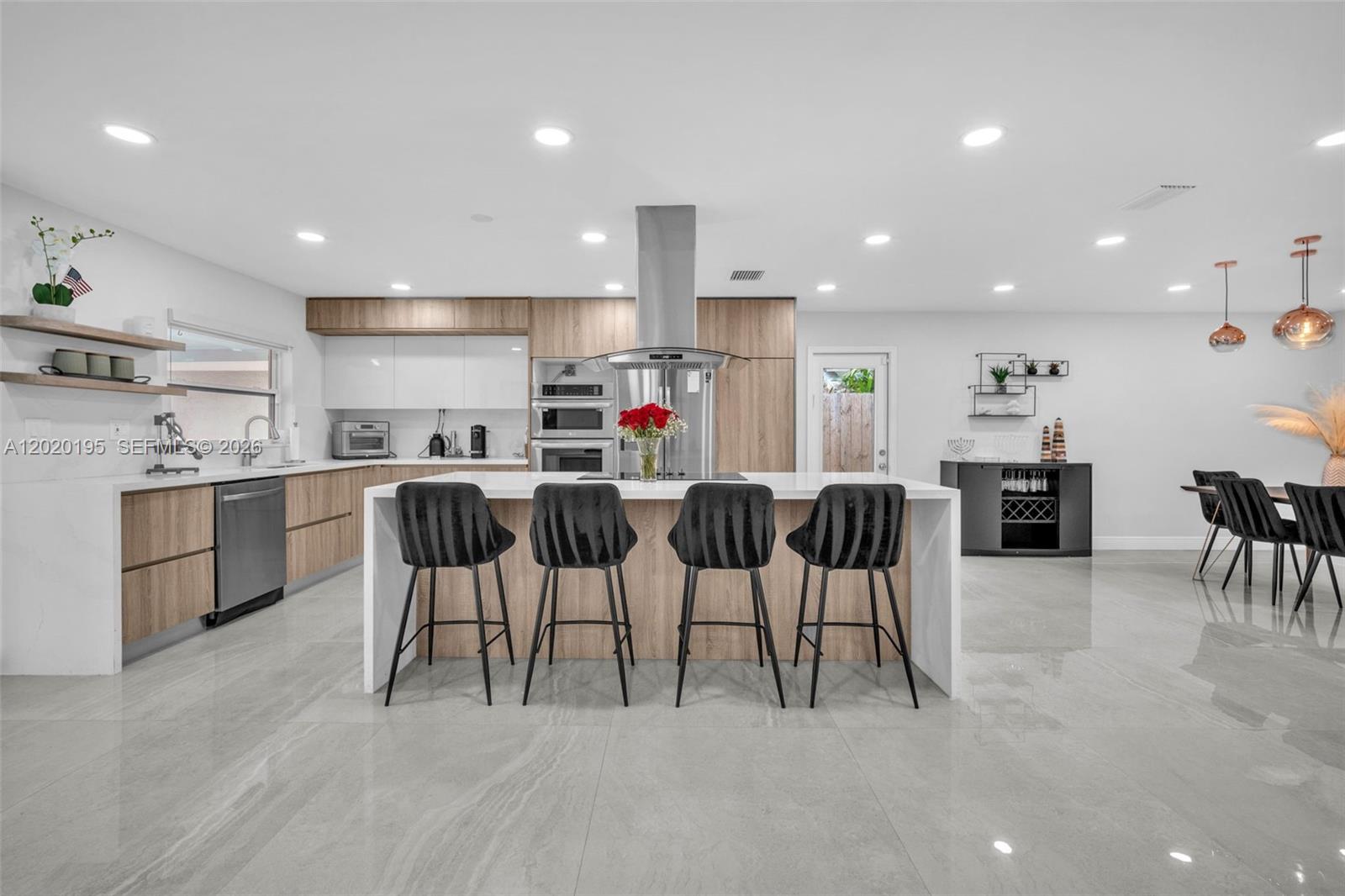 A modern kitchen features a large island with four stools, wood cabinetry, and tile flooring — 136 Greens Rd, Hollywood FL 33021, HOLLYWOOD, FL