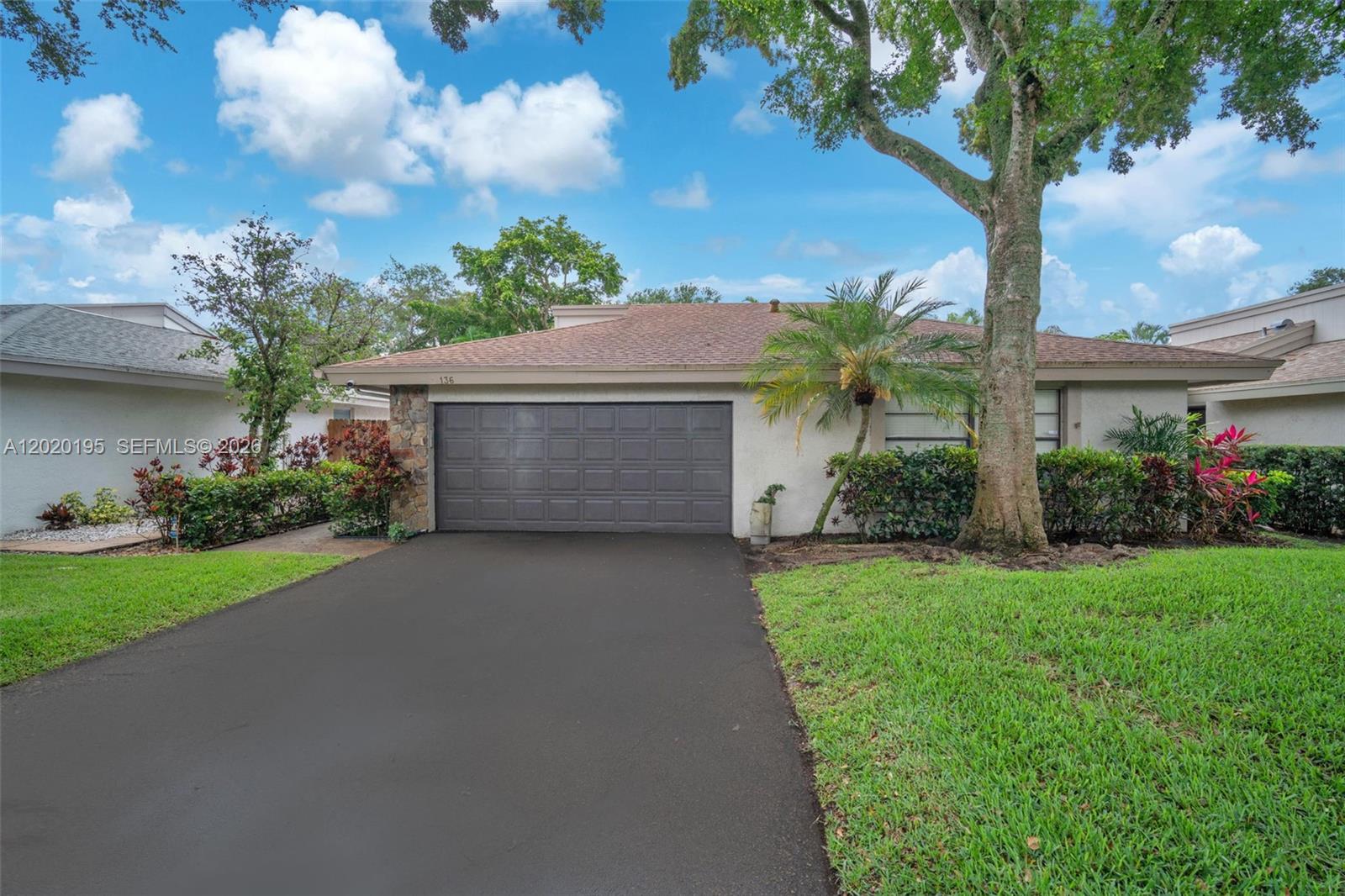 A single-story house features a dark garage door, a paved driveway, and a large tree — 136 Greens Rd, Hollywood FL 33021, HOLLYWOOD, FL