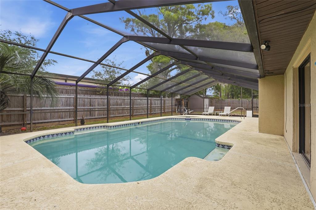 A screened-in swimming pool with a concrete deck and a wooden privacy fence — 7306 SW 17TH PLACE, GAINESVILLE, FL