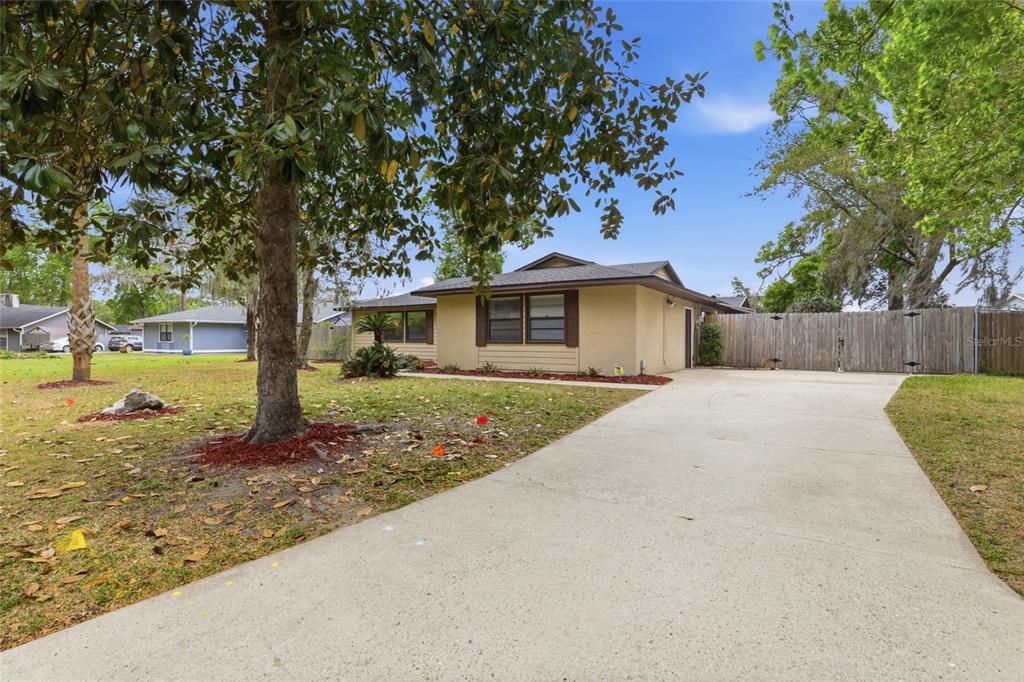 A single-story house with a concrete driveway, tan siding, and a wooden privacy fence — 7306 SW 17TH PLACE, GAINESVILLE, FL
