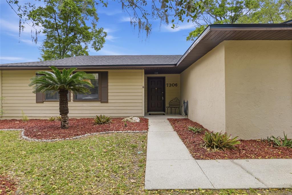 The exterior of a single-story house features beige siding, a dark door, and a walkway — 7306 SW 17TH PLACE, GAINESVILLE, FL