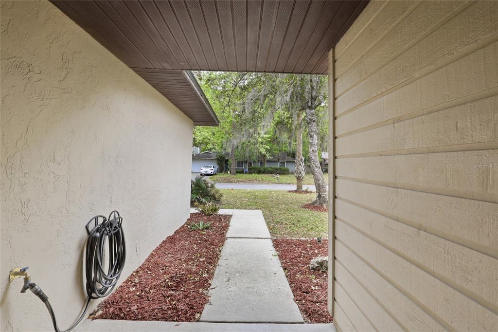 A concrete walkway leads from a covered entryway toward a residential street with trees — 7306 SW 17TH PLACE, GAINESVILLE, FL