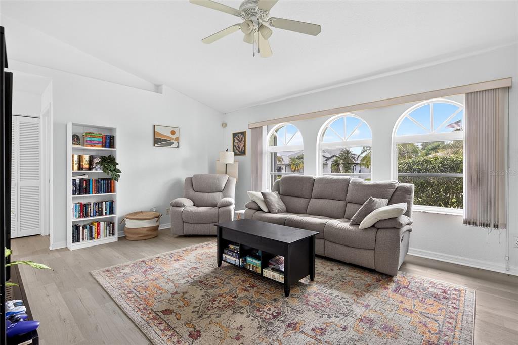 A living room with a gray sofa, recliner, bookshelf, and arched windows over wood flooring — 167 ALLWORTHY STREET, PORT CHARLOTTE, FL