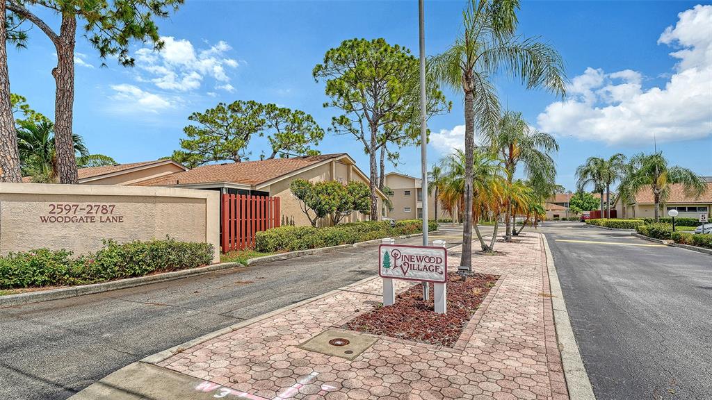 A street view shows the entrance to a residential community with a brick-paved walkway — 2763 WOODGATE LANE UNIT 104, SARASOTA, FL