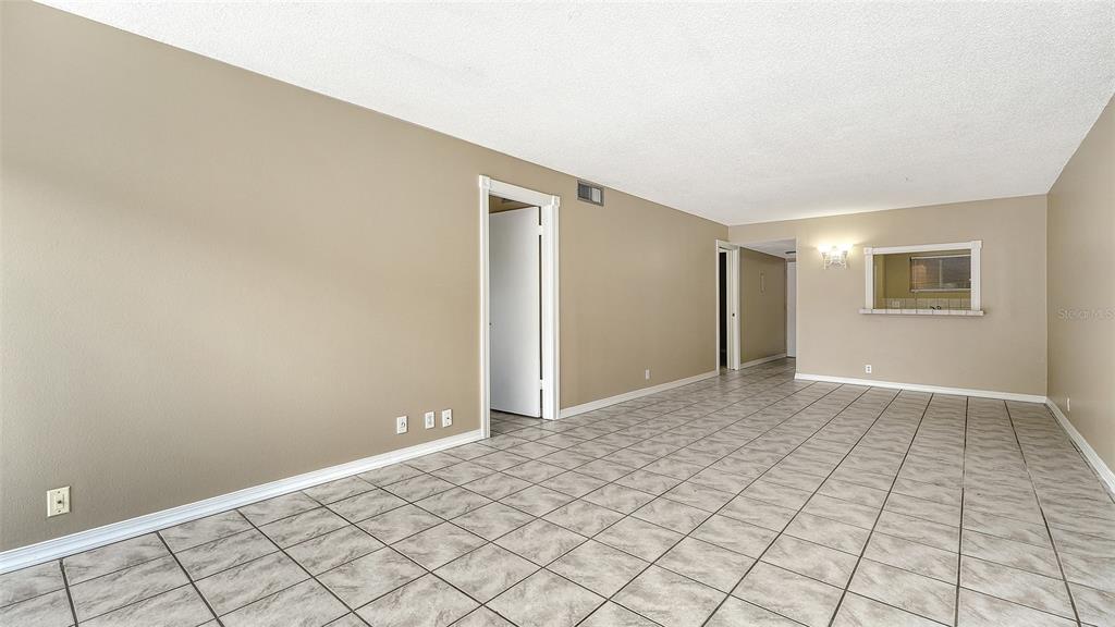 An empty room with beige walls, white trim, and light-colored square floor tiles — 2763 WOODGATE LANE UNIT 104, SARASOTA, FL