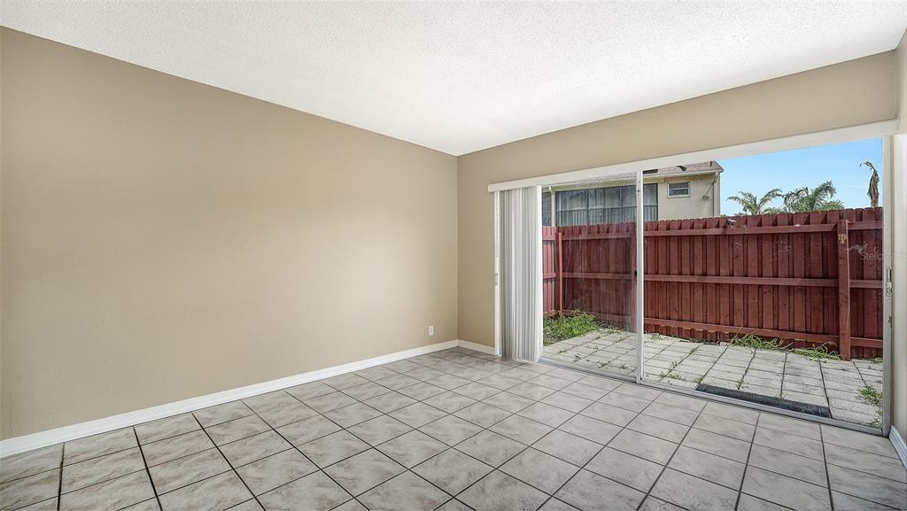 An empty room with beige walls, tiled flooring, and a sliding glass door to a patio — 2763 WOODGATE LANE UNIT 104, SARASOTA, FL