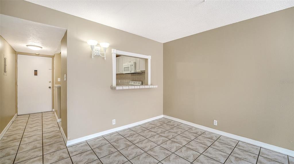 A dining area with tiled floors, beige walls, and a pass-through window to the kitchen — 2763 WOODGATE LANE UNIT 104, SARASOTA, FL