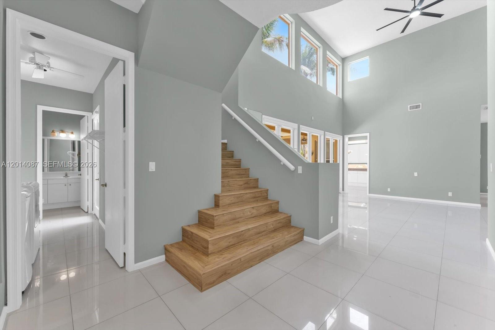 A modern interior features a wooden staircase, gray walls, and white tile flooring — 3728 NE 208th Ter, Aventura FL 33180, AVENTURA, FL