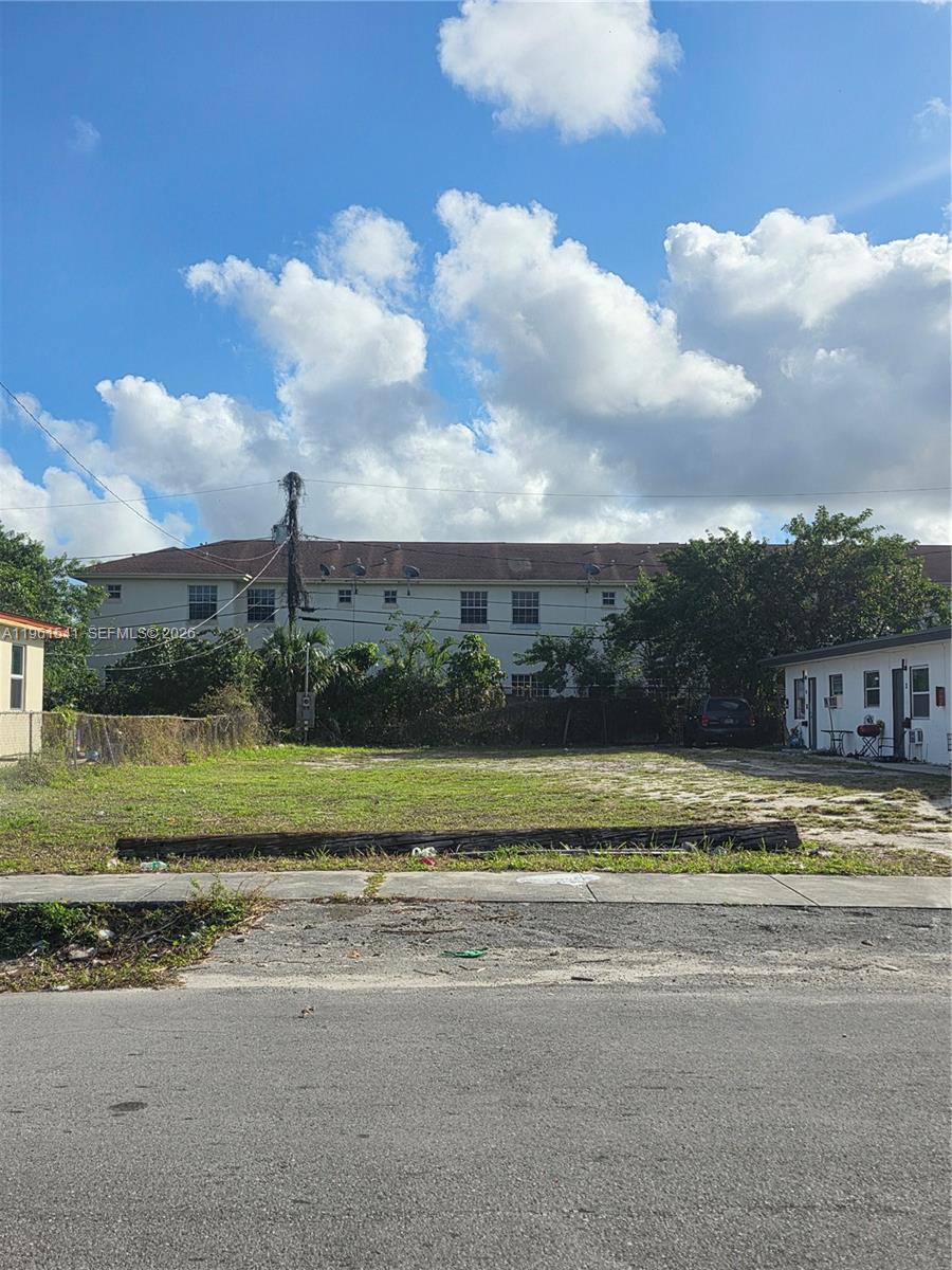 A vacant, grassy rectangular lot sits between two buildings under a cloudy blue sky — 10 Nw St, Hallandale Beach FL 33009, HALLANDALE BEACH, FL