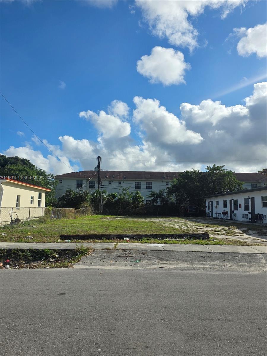 A vacant, grassy lot sits between two residential buildings under a blue sky with clouds — 10 Nw St, Hallandale Beach FL 33009, HALLANDALE BEACH, FL