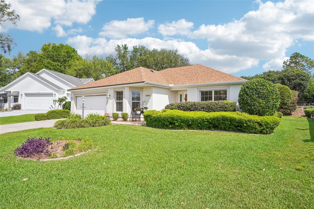 A single-story house with a tan roof, white stucco exterior, and a manicured front lawn — 16596 SE 77TH NORTHRIDGE COURT, THE VILLAGES, FL