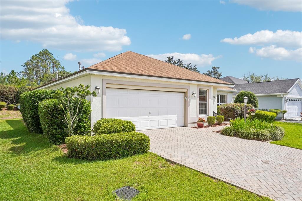 A single-story house with a white garage door, tan roof, and a paved driveway — 16596 SE 77TH NORTHRIDGE COURT, THE VILLAGES, FL
