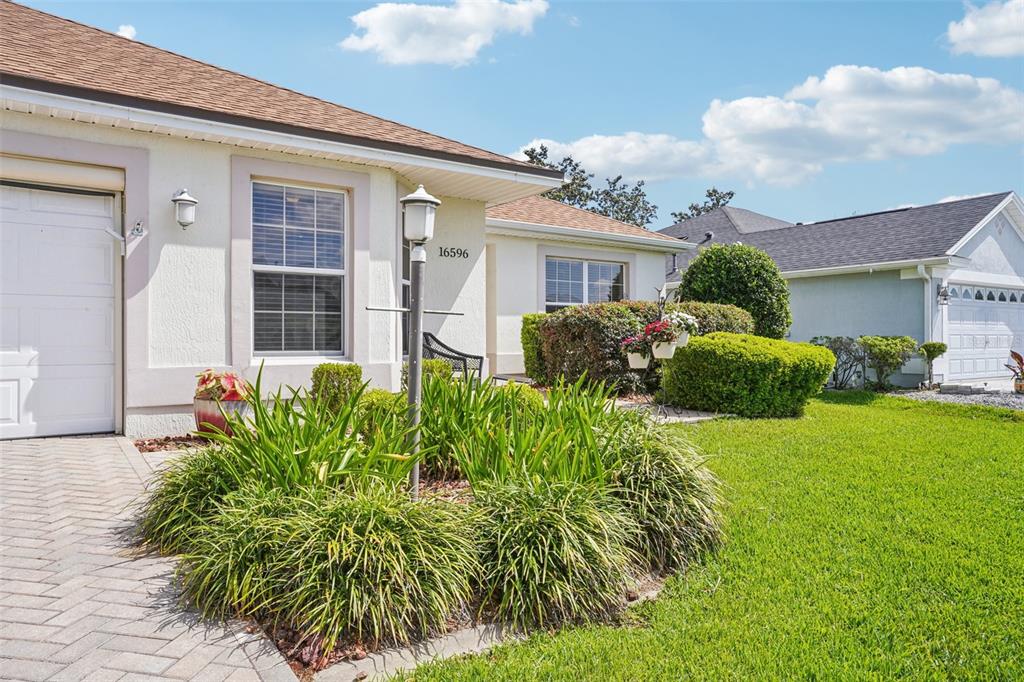 A single-story house with a paved driveway, a front garden, and a white garage door — 16596 SE 77TH NORTHRIDGE COURT, THE VILLAGES, FL