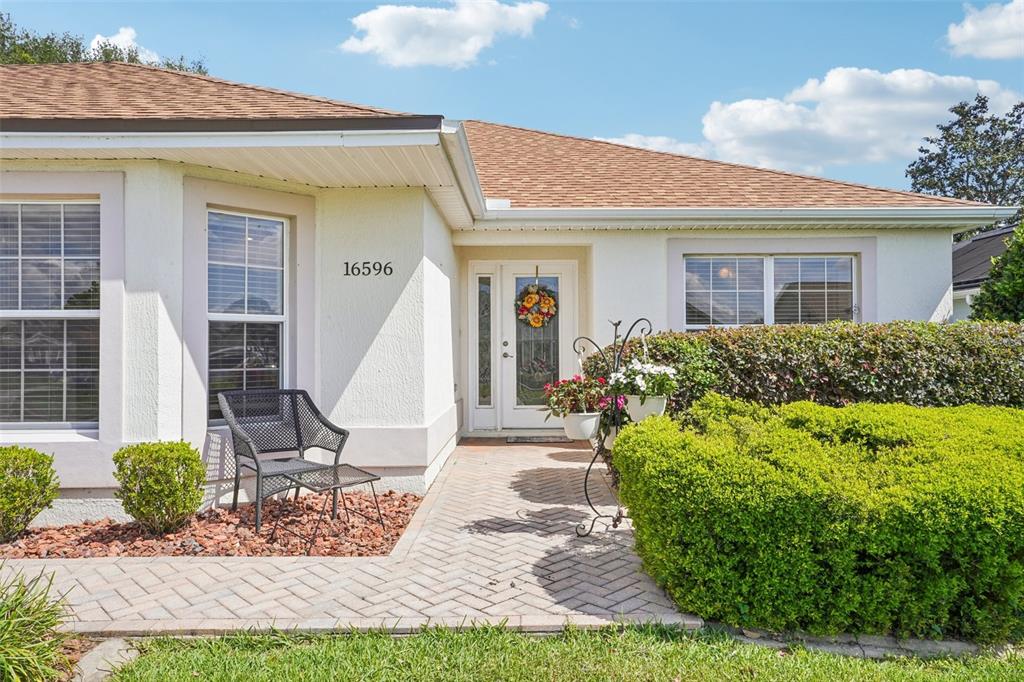A single-story house exterior features a brick walkway, a front door, and manicured landscaping — 16596 SE 77TH NORTHRIDGE COURT, THE VILLAGES, FL