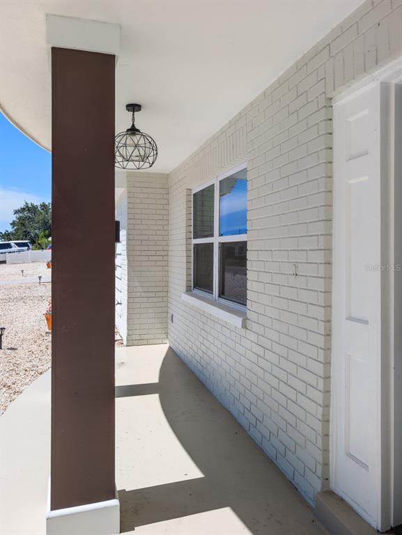 A covered porch features a brown support column, a pendant light, and white brick walls — 3650 KINGSBURY DRIVE, HOLIDAY, FL