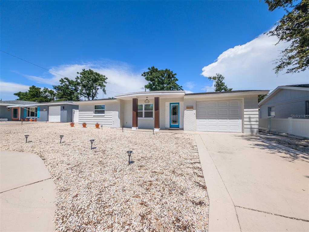 A single-story house with a white brick exterior, a garage, and a gravel front yard — 3650 KINGSBURY DRIVE, HOLIDAY, FL