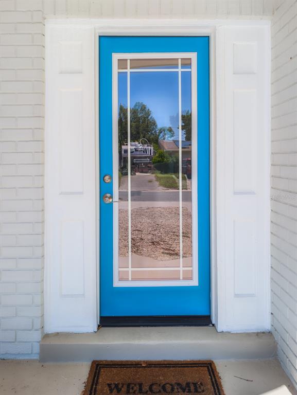 A bright blue front door with a glass panel is set between white brick walls — 3650 KINGSBURY DRIVE, HOLIDAY, FL
