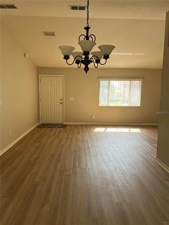 A spacious room features light wood-look flooring, a chandelier, a front door, and a window — 6035 SW 98TH STREET ROAD, OCALA, FL