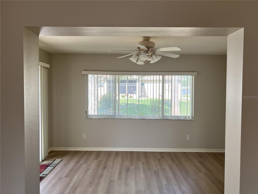 An empty room features light-colored wood-look flooring, a ceiling fan, and a large window — 6035 SW 98TH STREET ROAD, OCALA, FL