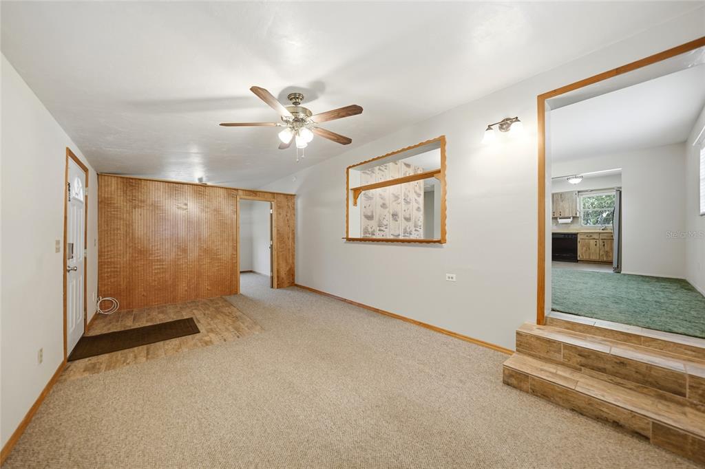A living room features wood paneling, carpeted flooring, a ceiling fan, and a step-up kitchen — 5549 SW SHORES AVENUE, ARCADIA, FL