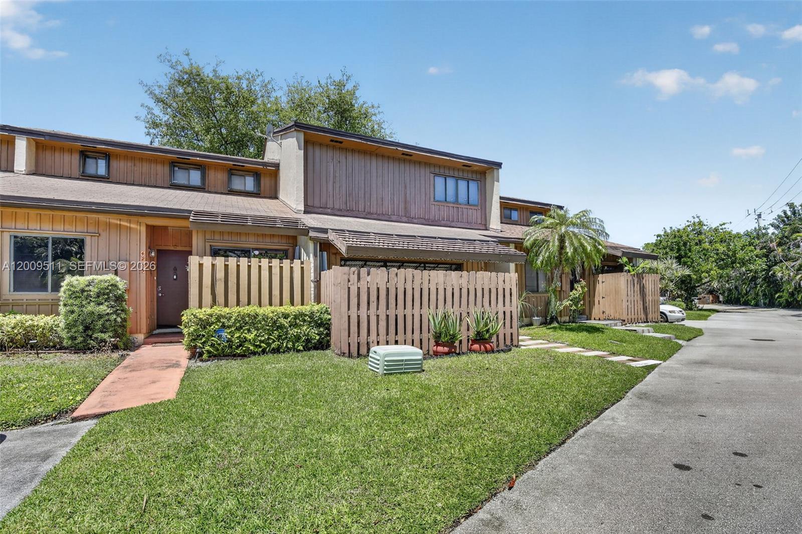 A two-story townhouse with brown wood siding, a fenced front yard, and a paved driveway — 4283 S Pine Island Rd, Davie FL 33328, DAVIE, FL