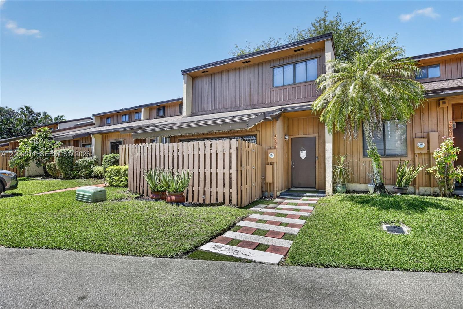 A two-story townhouse with vertical wood siding, a private fenced patio, and a paved walkway — 4283 S Pine Island Rd, Davie FL 33328, DAVIE, FL