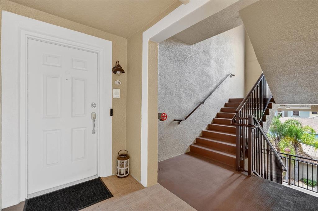 A white front door sits next to an outdoor staircase with brown steps and railings — 424 LUNA BELLA LANE UNIT 330, NEW SMYRNA BEACH, FL