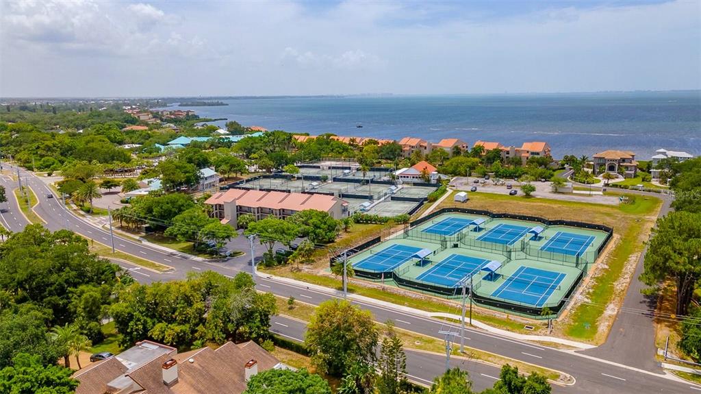An aerial view shows tennis courts, a multi-story building, and a road near the water — 4510 EL CONQUISTADOR PARKWAY UNIT 105, BRADENTON, FL