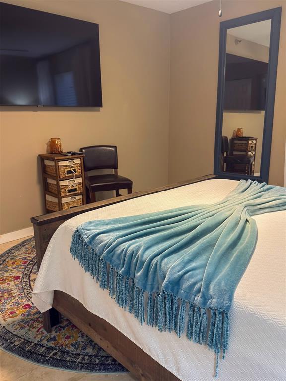 A bedroom features a bed with a blue throw blanket, a wall-mounted television, and a mirror — 4510 EL CONQUISTADOR PARKWAY UNIT 105, BRADENTON, FL