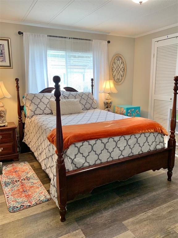 A bedroom features a four-poster wooden bed, patterned bedding, and wood-look flooring — 2122 OAK GROVE DRIVE UNIT 79, ZELLWOOD, FL