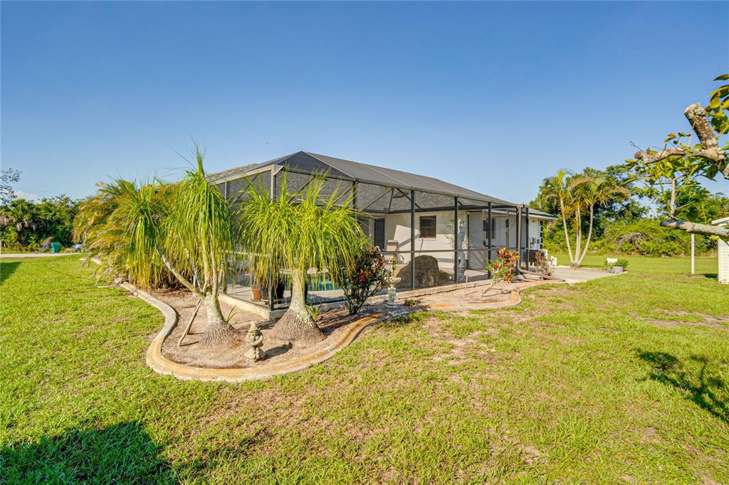 The exterior of a house features a screened-in pool enclosure and landscaped garden beds — 12038 FLORENCE AVENUE, PORT CHARLOTTE, FL