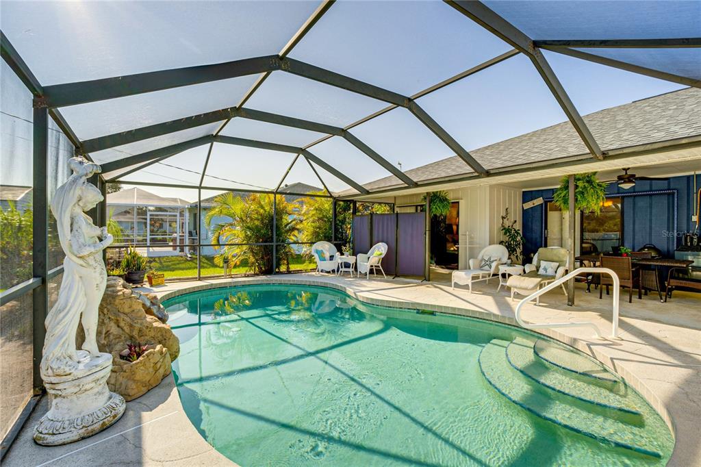A screened-in swimming pool patio features a statue, lounge chairs, and a dining area — 12038 FLORENCE AVENUE, PORT CHARLOTTE, FL
