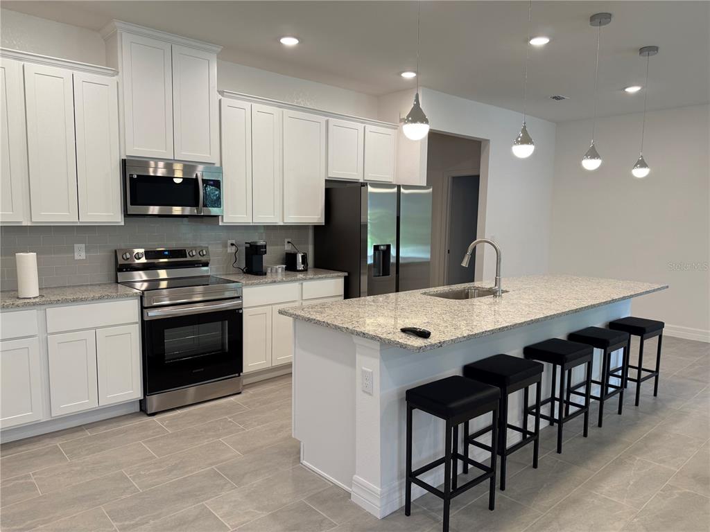 A modern kitchen features white cabinets, granite countertops, stainless steel appliances, and a large island — 15467 MAYNARD AVENUE, PORT CHARLOTTE, FL