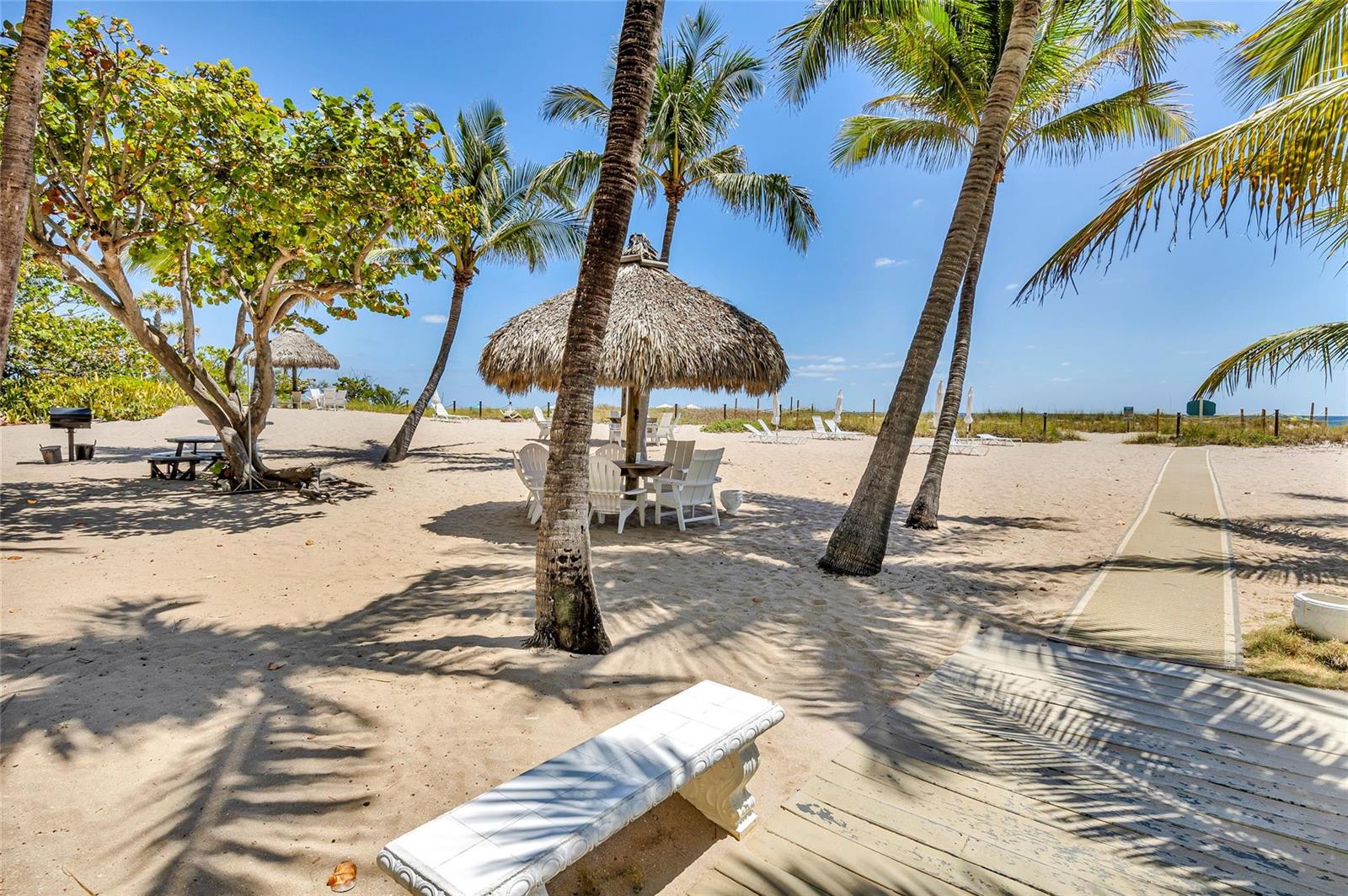 A sandy beach area features a thatched-roof tiki hut, palm trees, and a wooden walkway — 710 N Ocean Boulevard # 312, Pompano Beach FL 33062, POMPANO BEACH, FL