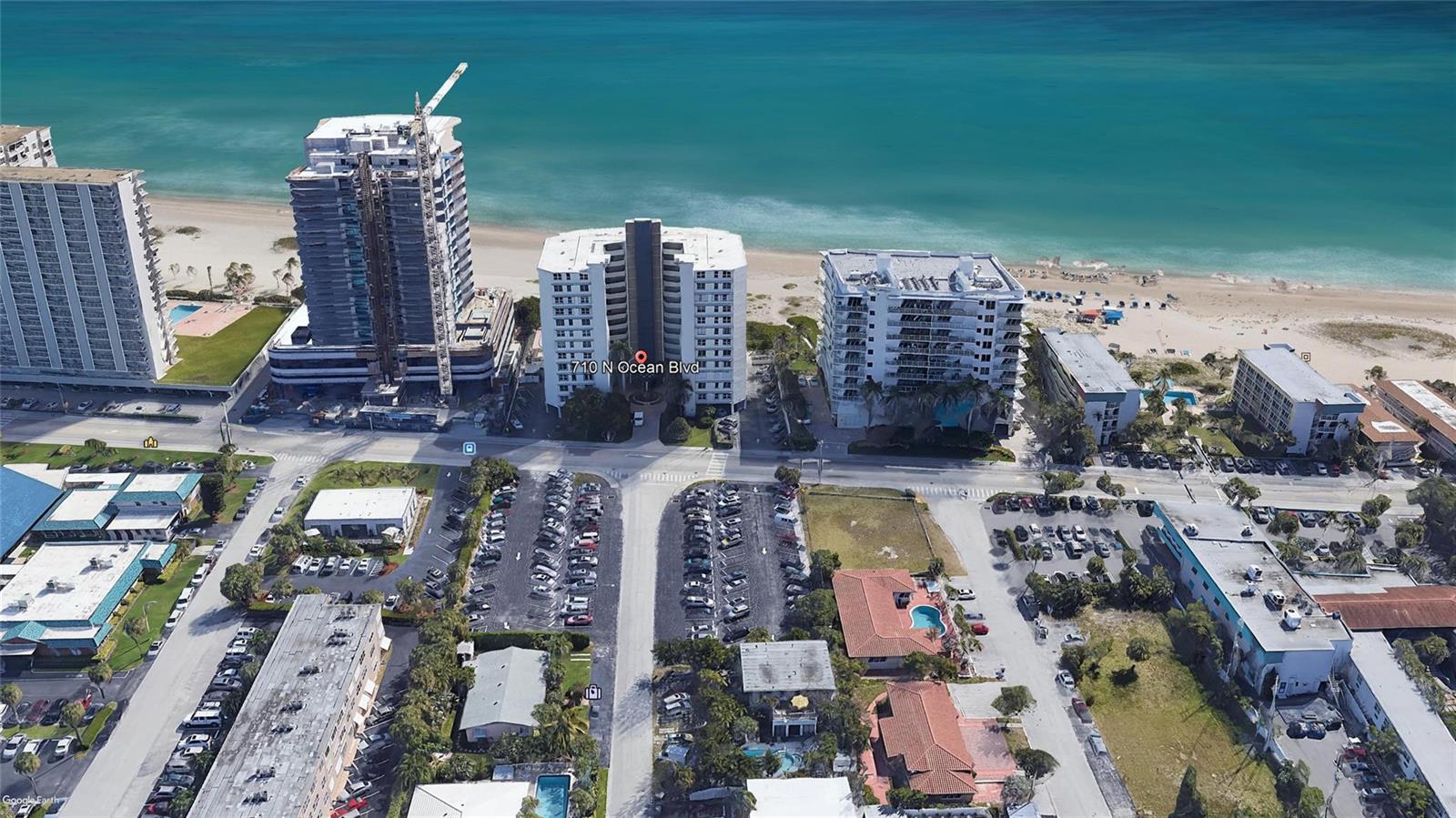An aerial view shows high-rise buildings along a sandy beach with parking lots in front — 710 N Ocean Boulevard # 312, Pompano Beach FL 33062, POMPANO BEACH, FL