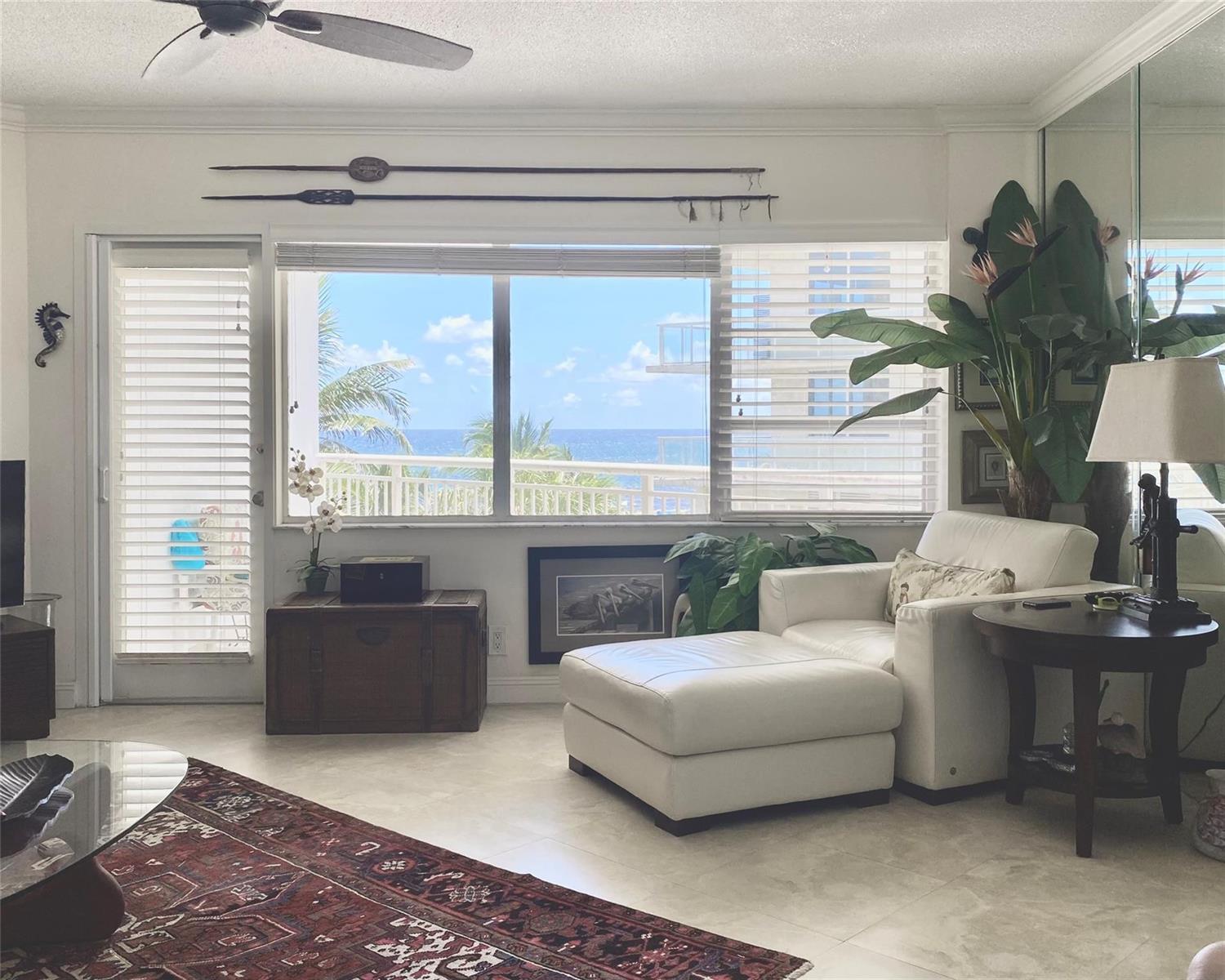 A living room features a white armchair, a wooden chest, and a view of the ocean — 710 N Ocean Boulevard # 312, Pompano Beach FL 33062, POMPANO BEACH, FL
