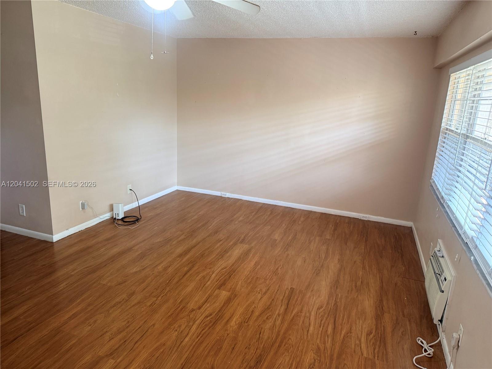 An empty room features light-colored walls, wood-look flooring, a ceiling fan, and a window — PEMBROKE PINES, FL