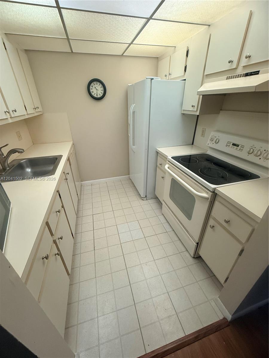 A galley kitchen features white cabinets, a white refrigerator, and a white electric range — PEMBROKE PINES, FL