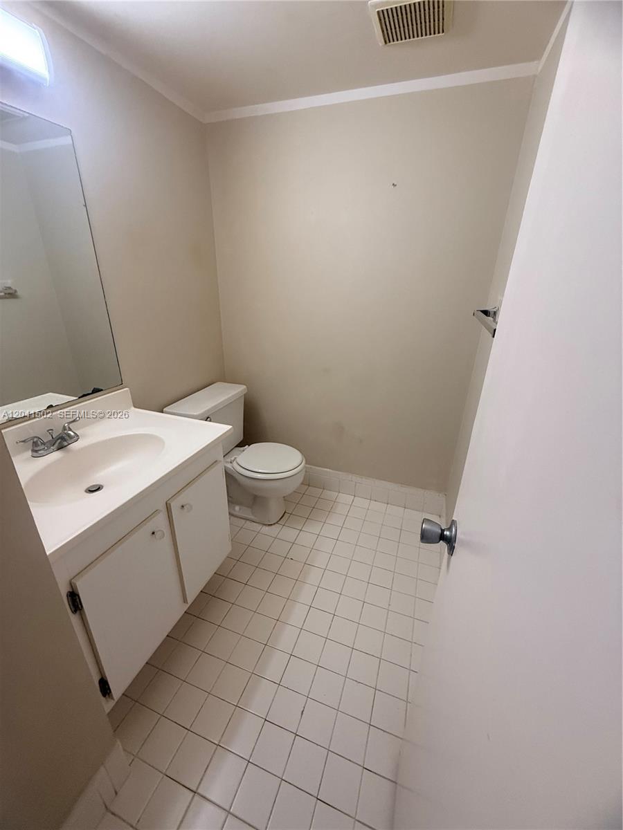 A small bathroom features a white vanity, a toilet, and white tiled flooring — PEMBROKE PINES, FL