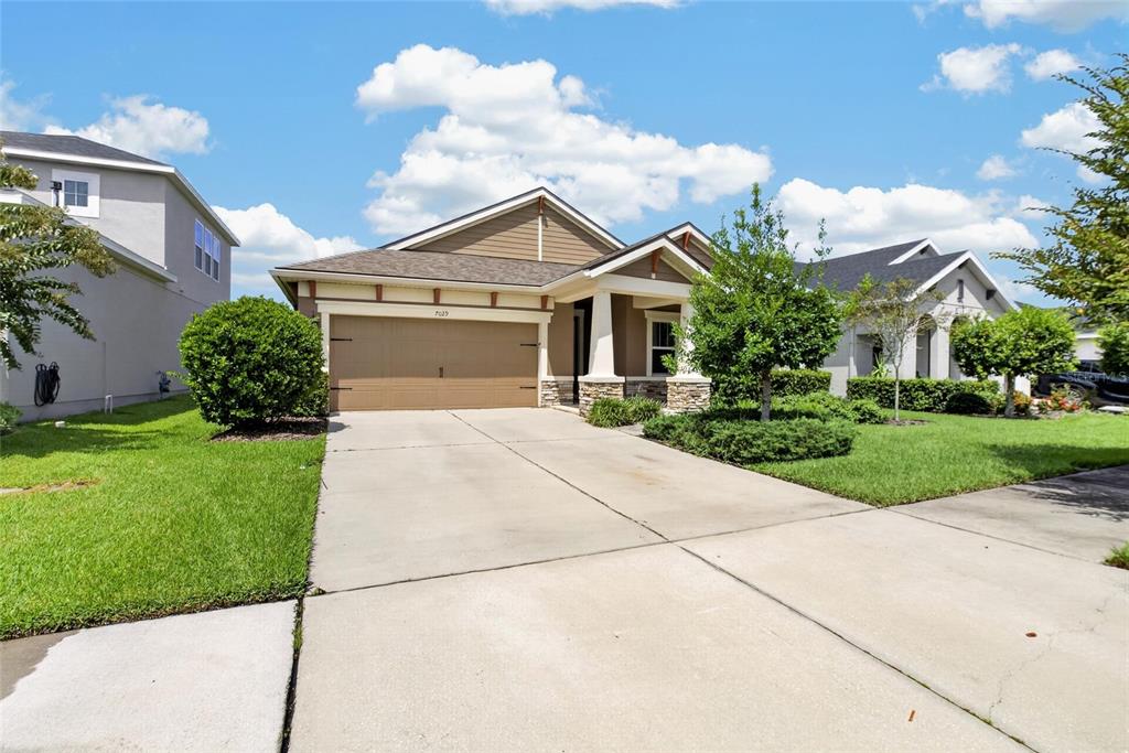 A single-story suburban house features a tan exterior, a two-car garage, and a concrete driveway — 7029 OLD BENTON DRIVE, APOLLO BEACH, FL