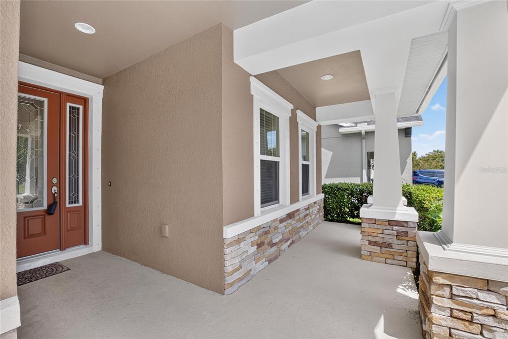 A covered front porch features a brown door, stone accents, and white support columns — 7029 OLD BENTON DRIVE, APOLLO BEACH, FL