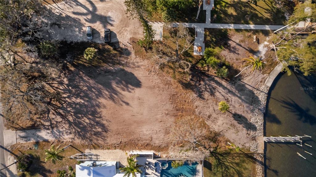 An aerial view shows a cleared, vacant waterfront lot with trees and a nearby dock — 712 PALMA SOLA BOULEVARD, BRADENTON, FL