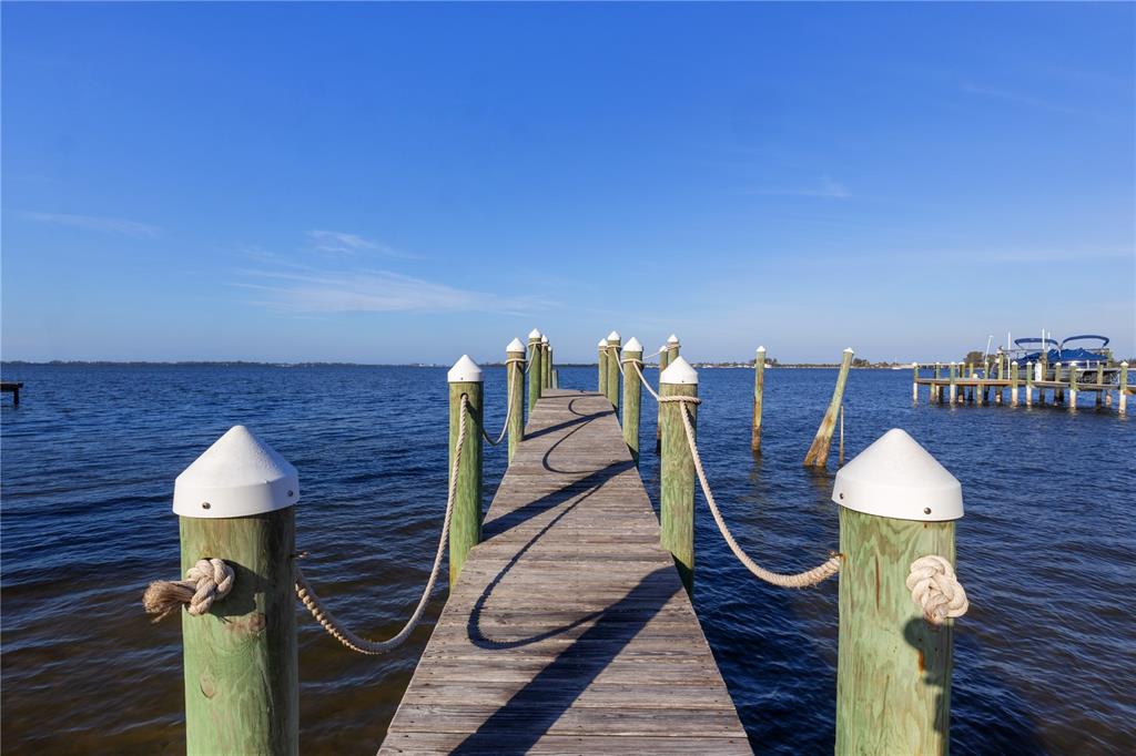 A wooden dock with white-capped pilings and rope railings extends into a calm body of water — 712 PALMA SOLA BOULEVARD, BRADENTON, FL