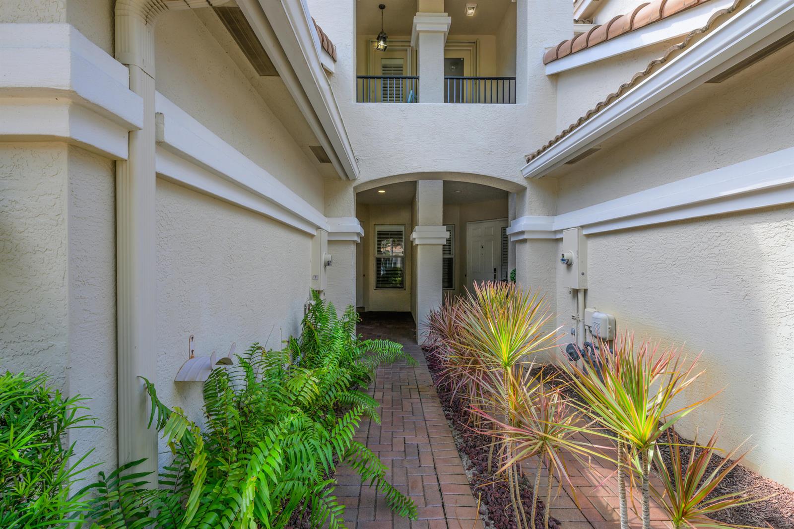 A brick walkway leads through a covered entryway between two stucco walls with landscaping — 742 Cable Beach Lane, West Palm Beach FL 33410, WEST PALM BEACH, FL