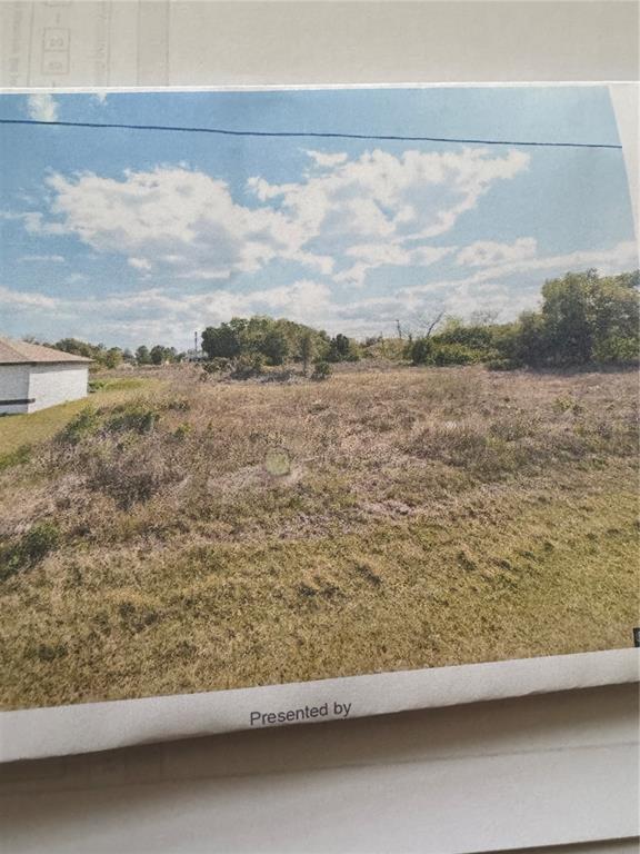 A vacant, grassy lot sits next to a house under a blue sky with clouds — 4215 8TH ST SW, LEHIGH ACRES, FL